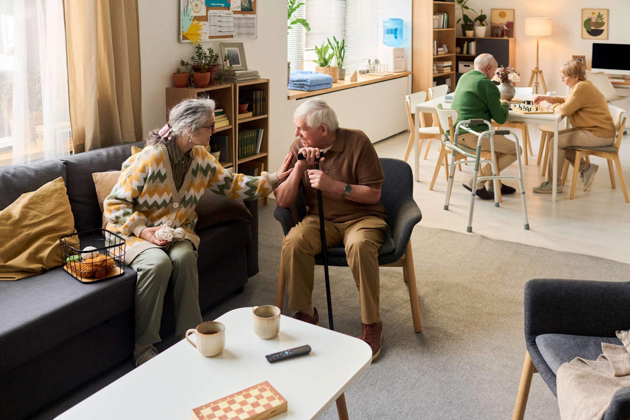 residents-socializing Residents socializing in a common area, chatting on a couch while others play chess nearby.